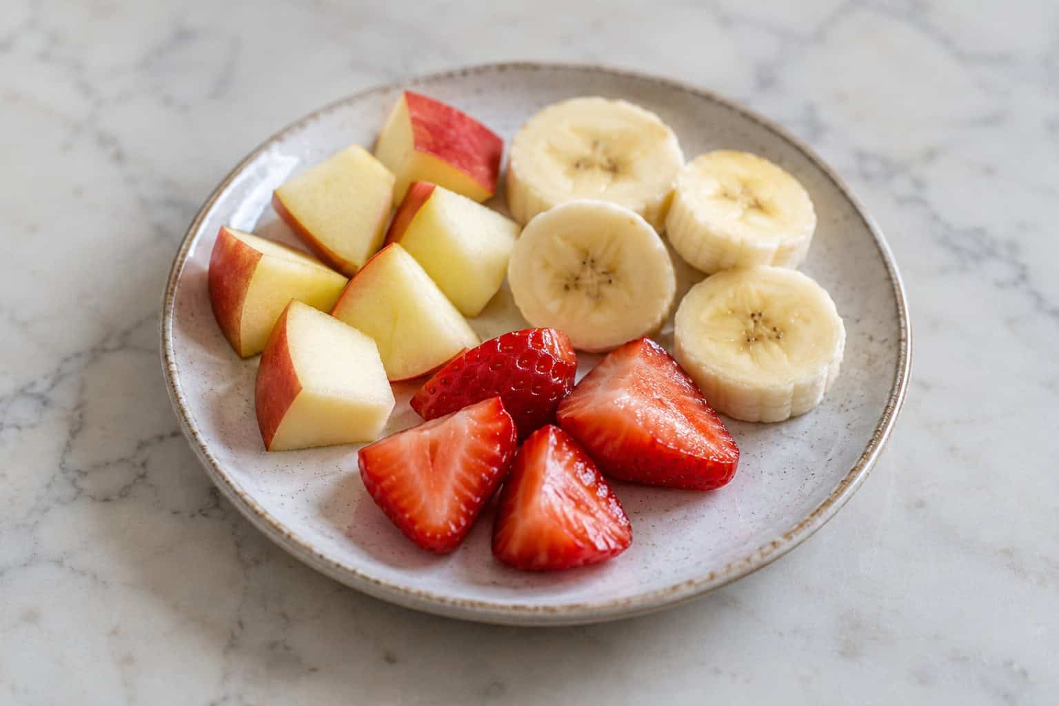 Kleine stukjes appel, banaan en aardbei op een bordje.