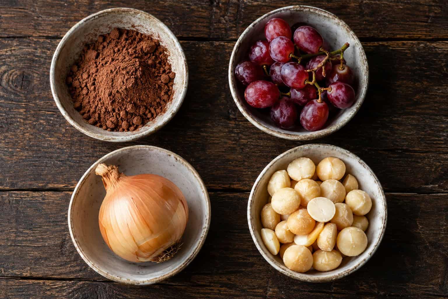 Schaaltjes met cacao, druiven, ui en macadamianoten op een tafel.